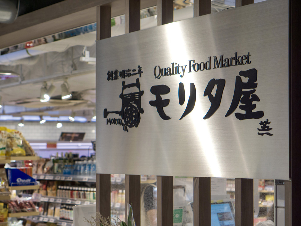 スーパー「モリタ屋」の店内入口付近にある、金属製の大きな看板