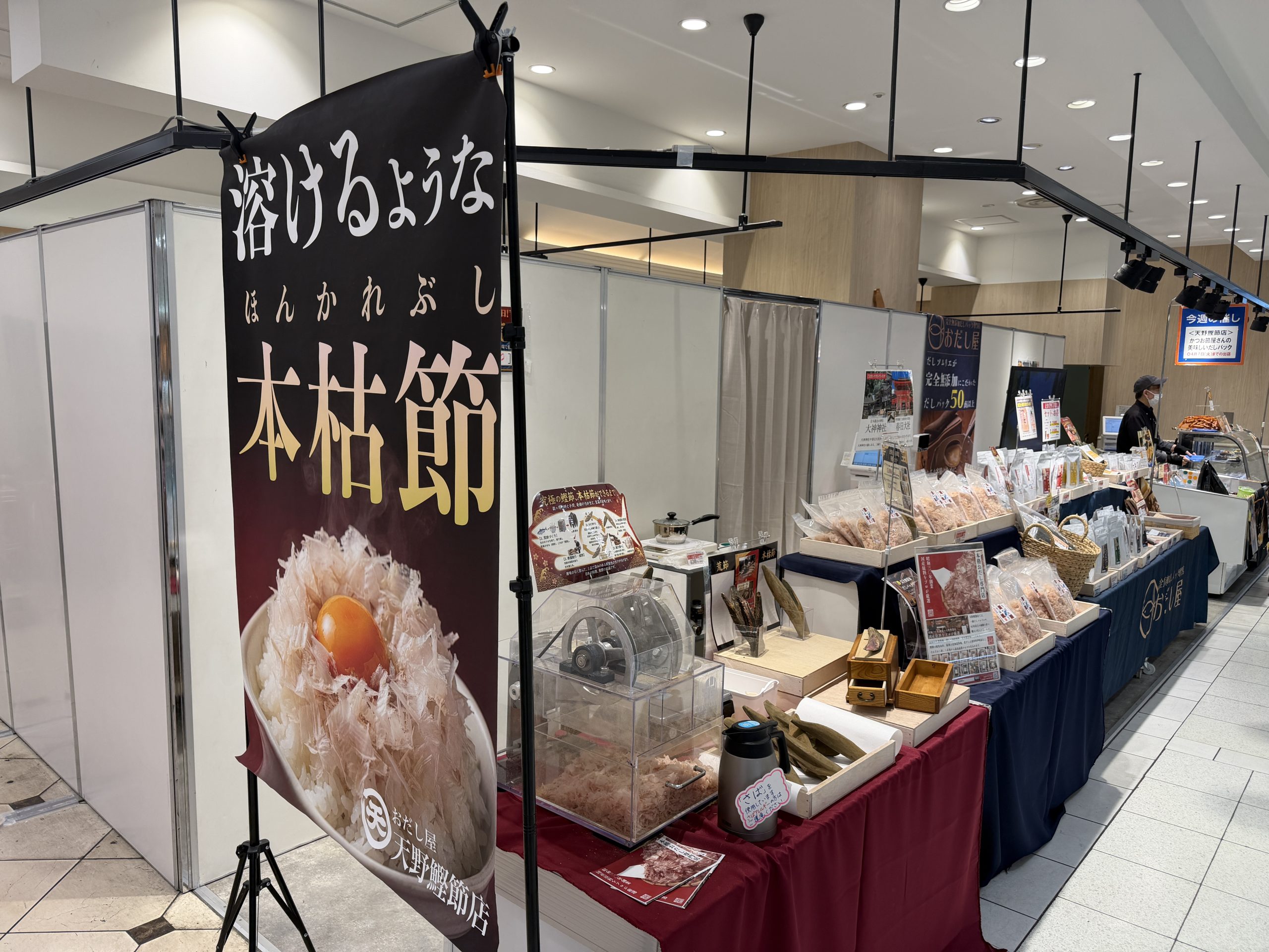 百貨店の催事場に出店した鰹節屋の売り場。『溶けるような本枯節』の大きな旗や削り器、だし商品が並んでいます。