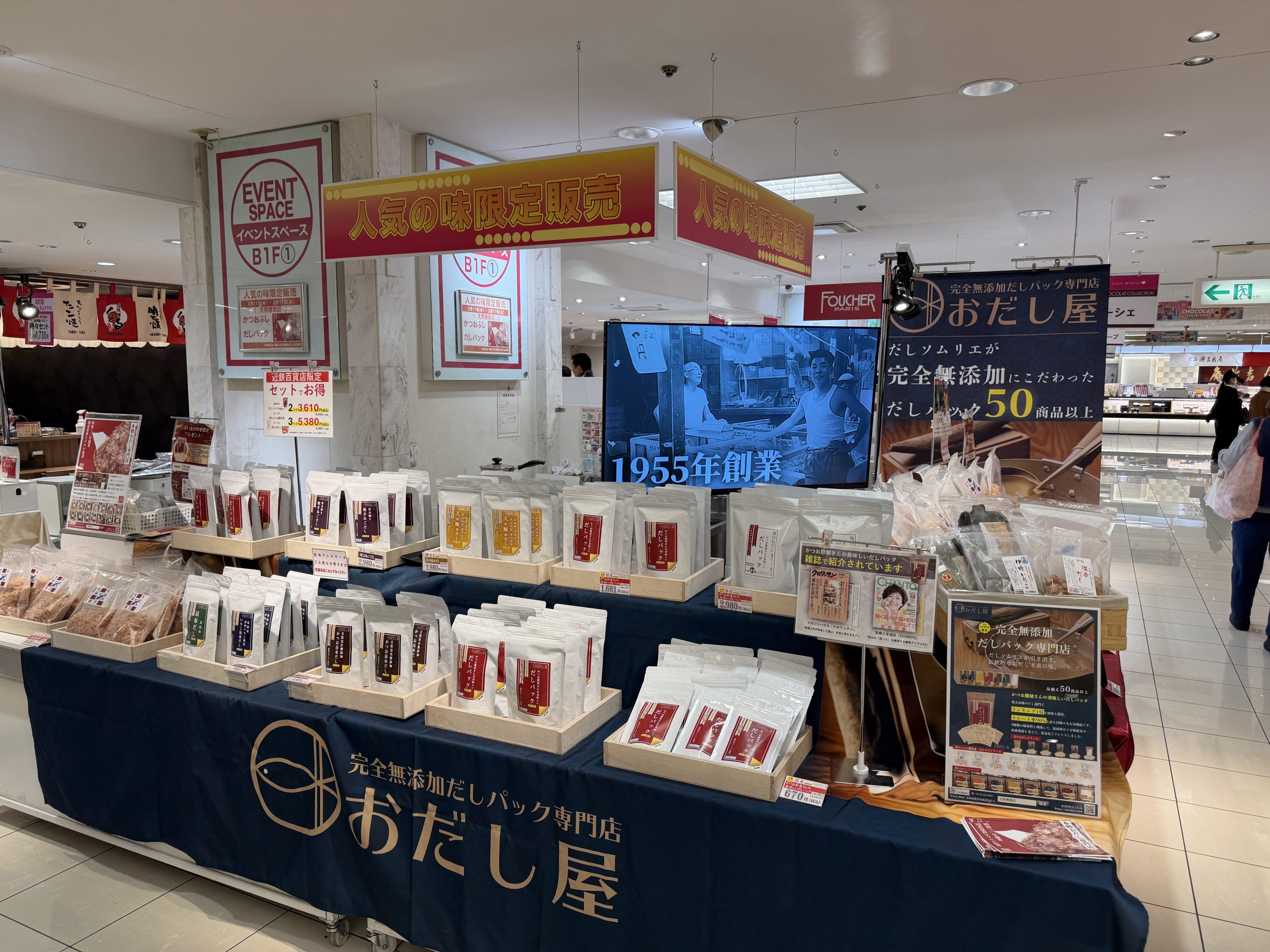 「おだし屋」の催事販売コーナー。無添加だしパックや削り節などの商品が整然と並び、店頭モニターや案内看板も設置されています。
