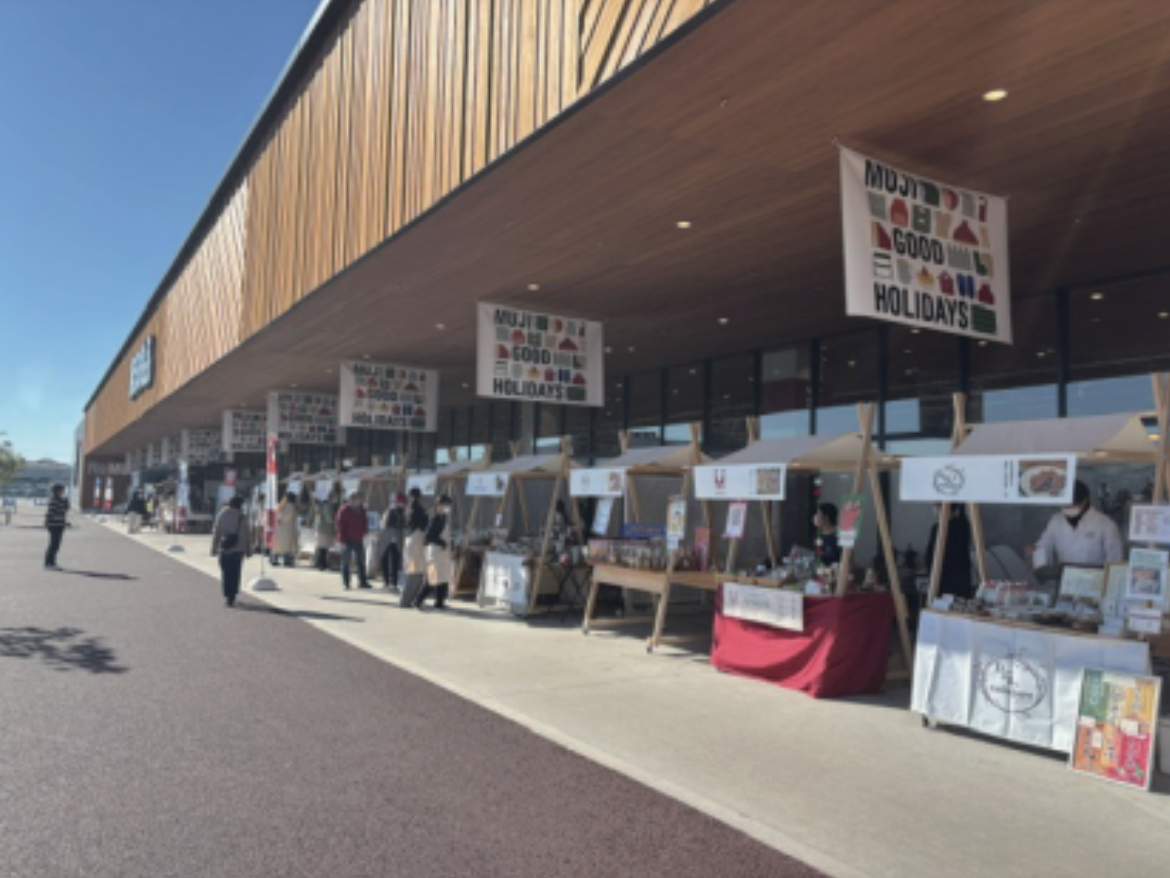 無印良品の店舗前に「GOOD HOLIDAYS」の屋外マルシェが並び、青空の下で多くのお客様が行き交っている様子。
