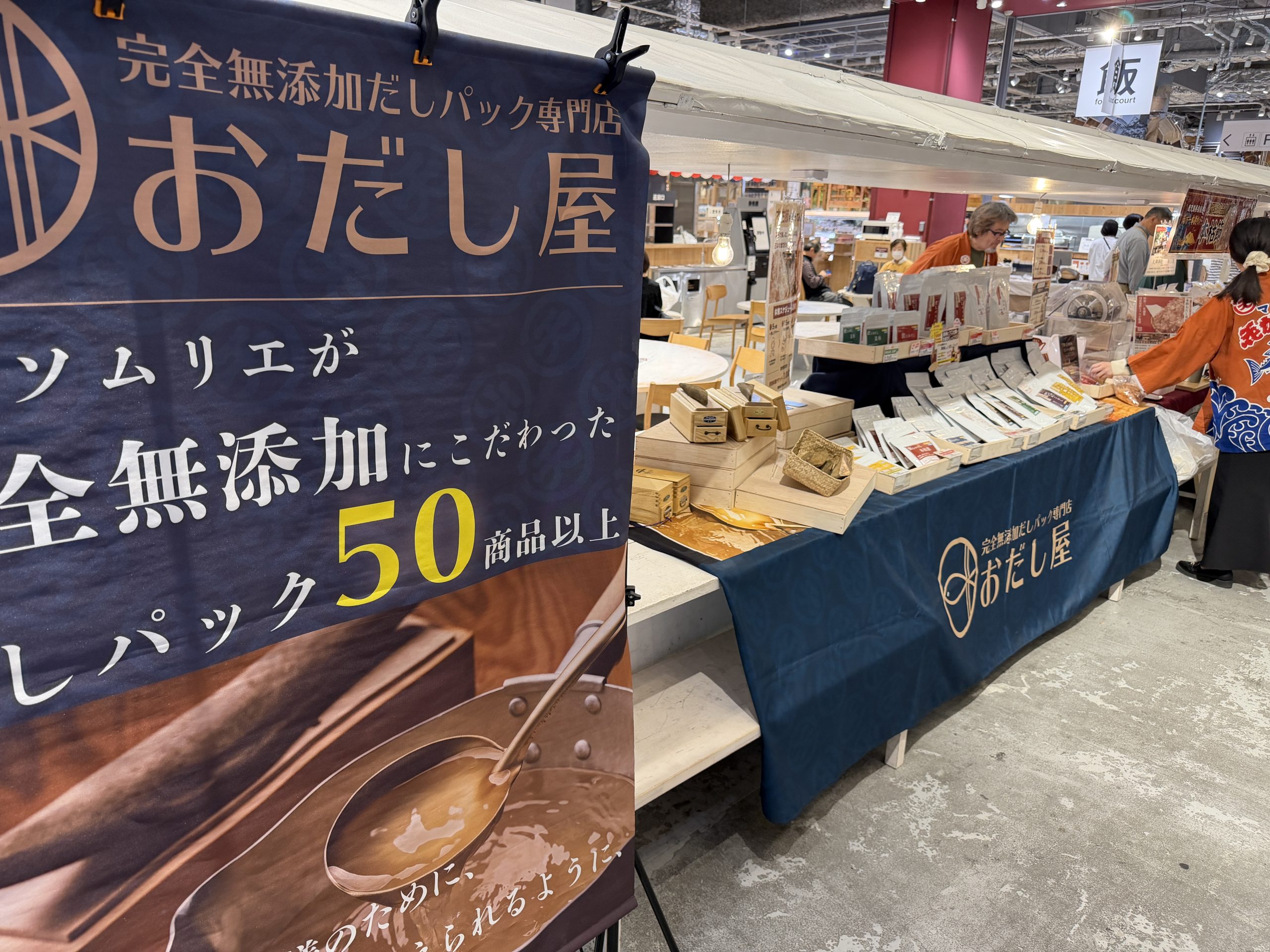屋内イベント会場に出店した「おだし屋」のブース。完全無添加だしパックの看板と、商品が並んだ販売台が写っている。