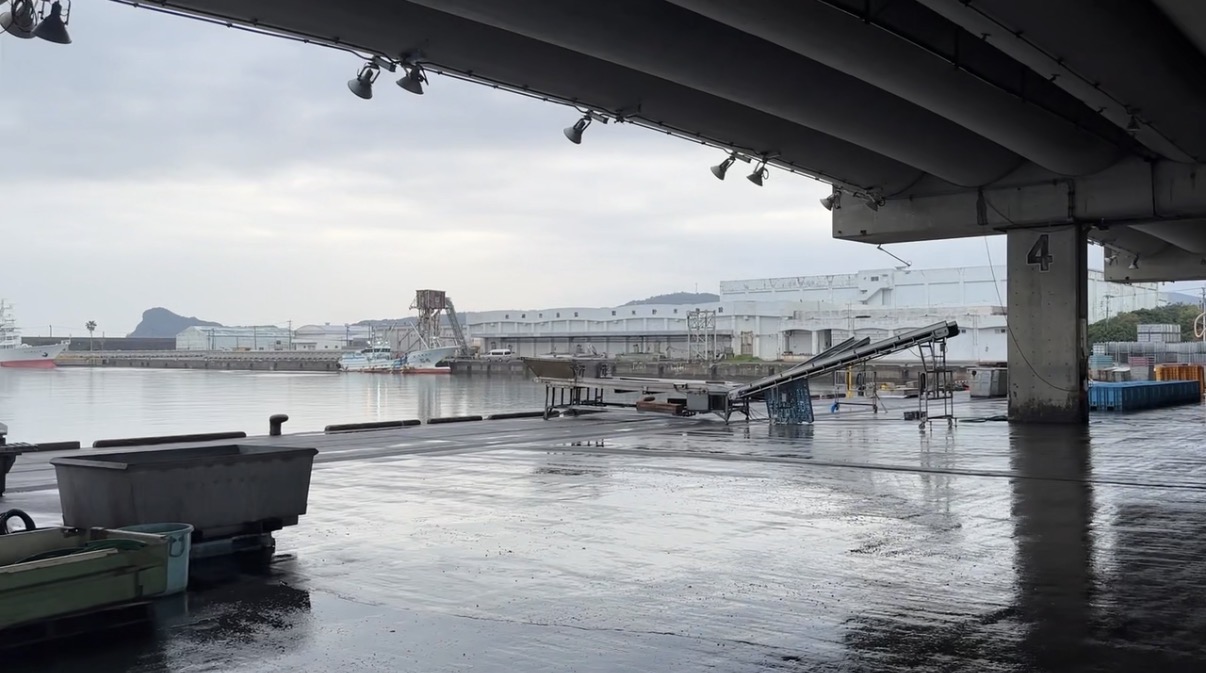 雨上がりの港の風景。屋根の下から、岸壁やコンベア、対岸の工場が見えています。